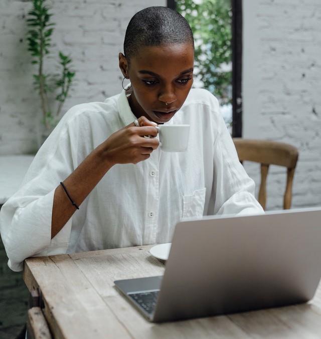 La mujer mira cuidadosamente la computadora portátil mientras toma café.
