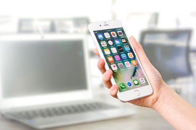 mano sostiene el iphone abierto en casa con varios iconos de aplicaciones